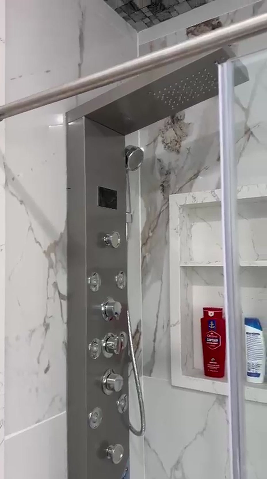 Stainless steel multi-jet shower panel with rainfall head installed against marble tile with a tiled niche in Toronto