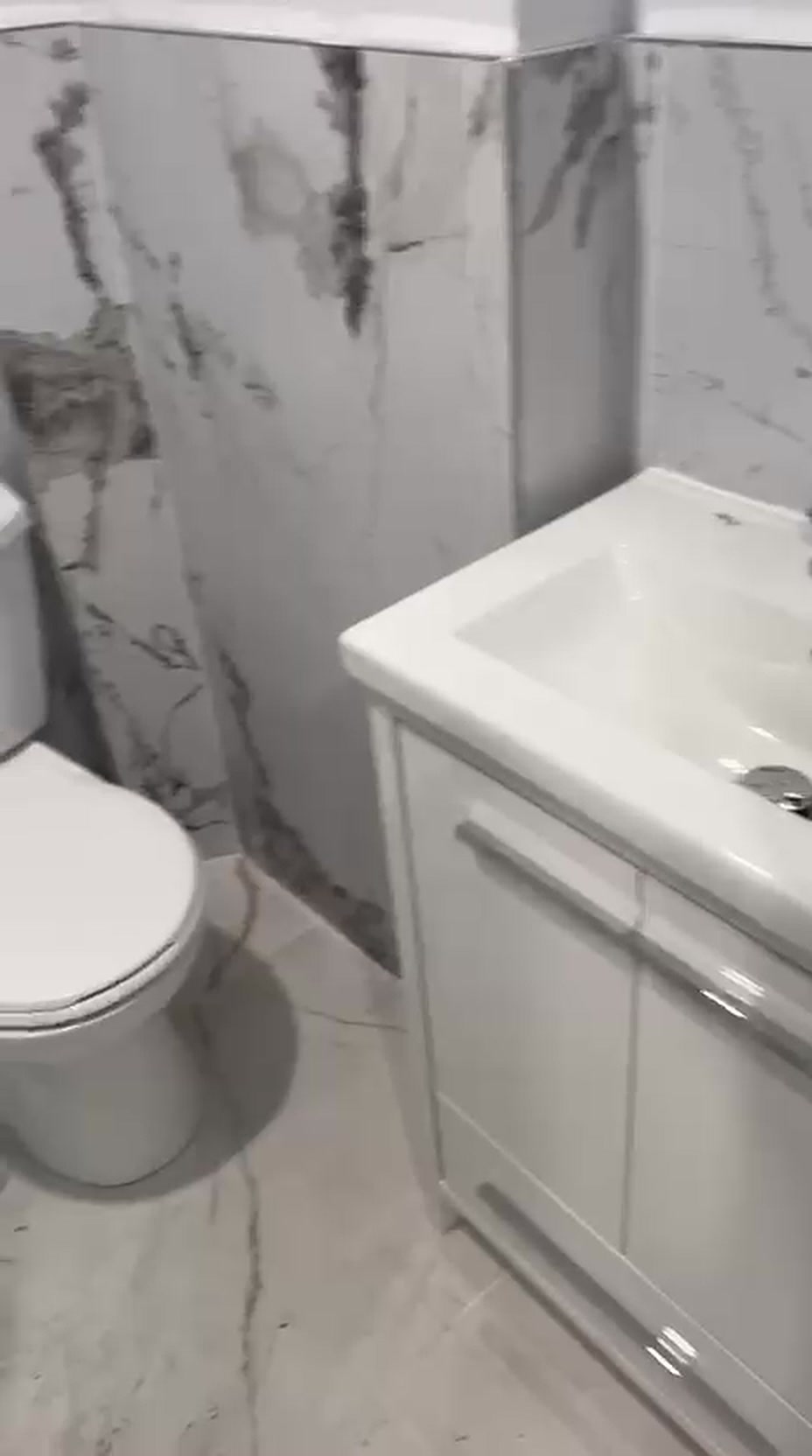 Compact Toronto bathroom renovation with marble tile walls, a white vanity with integrated sink and polished tile floor