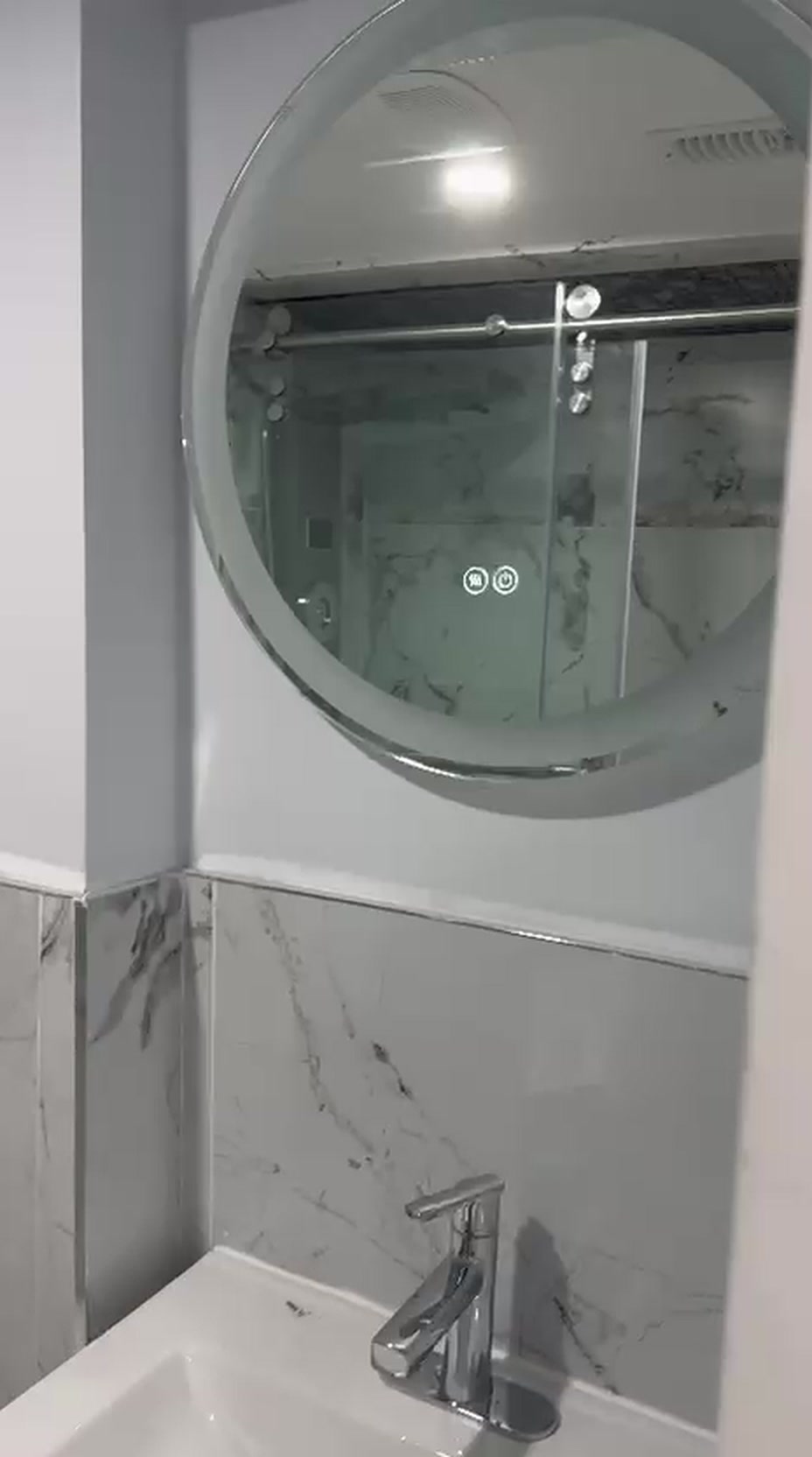 Backlit round LED mirror above a white vanity with chrome faucet and marble tile wainscot in a Toronto powder room